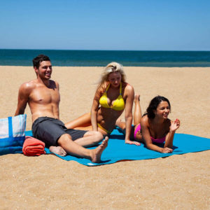 Tapis de plage bleu sur le sable , un homme, une femme et un enfant en maillot sur la serviette
