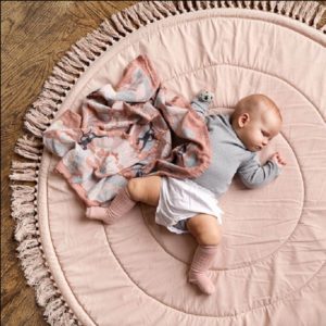tapis de sol rond et rose avec des franges et un bébé en barboteuse et un doudou rose