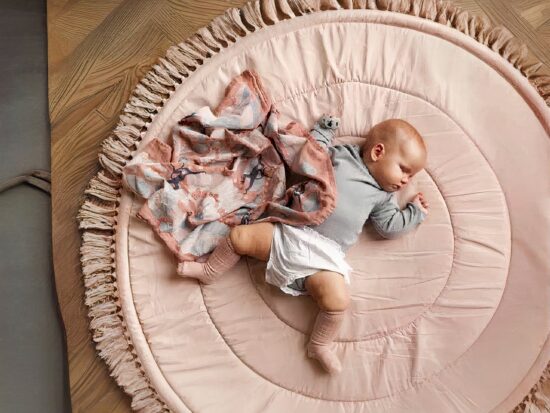 tapis de sol rond et rose avec des franges et un bébé en barboteuse et un doudou rose