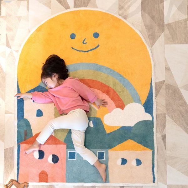 grand tapis coloré au motifs de maison et d'un arc en ciel avec une petite fille allongé dessus