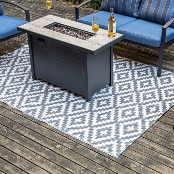 tapis de terrasse tissé avec motifs losanges gris et blanc , table basse noire et banquette bleu