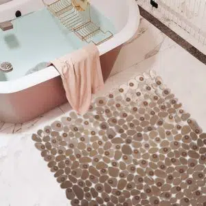 Tapis de salle de bain imitation galet doré et rebord de baignoire rose avec une serviette posé dessus