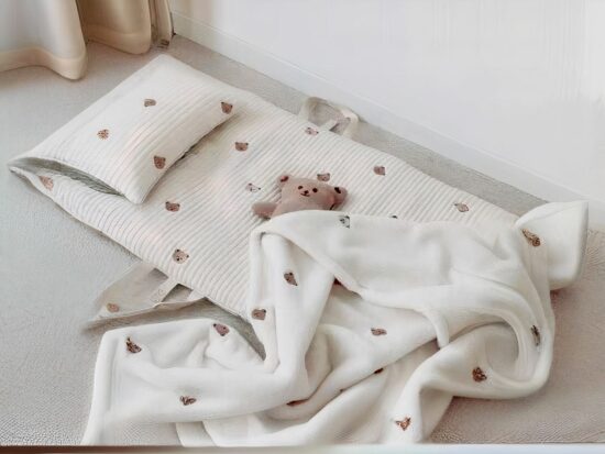 Tapis blanc avec coussin et couverture illustré d'une tête d'ourson