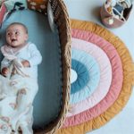 Petit tapis en demi cercle motif arc en ciel et un bébé dans son couffin
