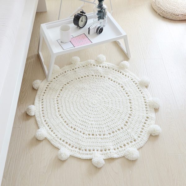 tapis rond blanc tricoté avec pompons et petite table basse blanche