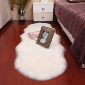 Tapis cocooning blanc style peau de bête installé au pied d'un lit dans une chambre avec des cadres posé dessus au sol
